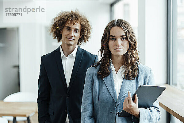 Junge Geschäftsfrau mit Tablet-PC steht vor einem Geschäftsmann im Büro