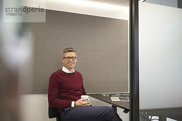 Lächelnder Geschäftsmann mit Kaffeetasse im Büro