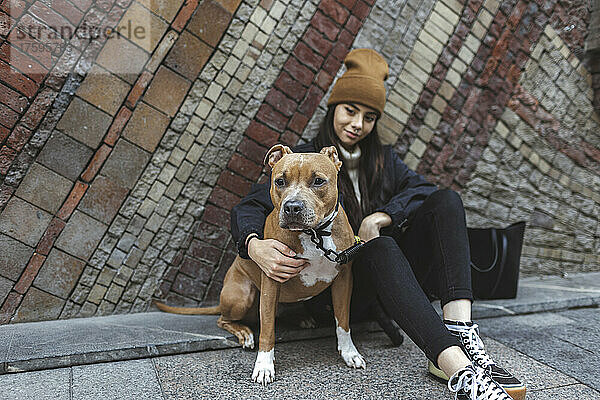 Junge Frau mit Hund sitzt vor der Wand
