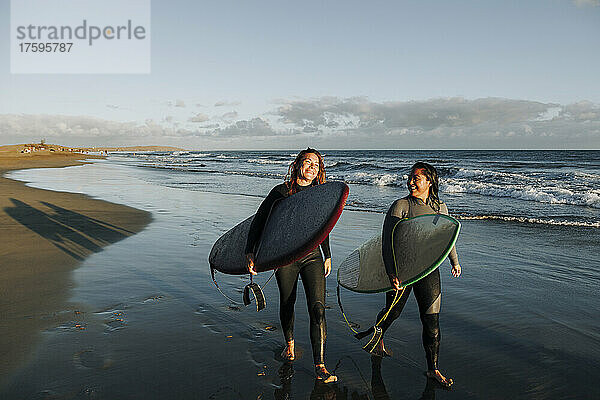 Frauen  die mit Surfbrettern in der Nähe des Meeres am Strand  Gran Canaria  Kanarische Inseln  spazieren gehen