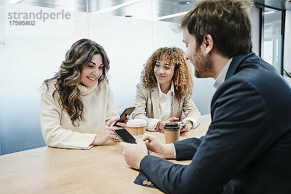 Lächelnde Geschäftsfrauen und Geschäftsmann mit Smartphones genießen die Kaffeepause