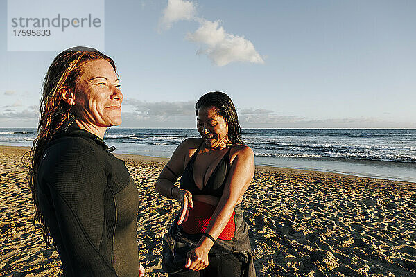 Lächelnde Frau in der Nähe eines Surfers  der den Neoprenanzug am Strand von Gran Canaria  Kanarische Inseln  auszieht