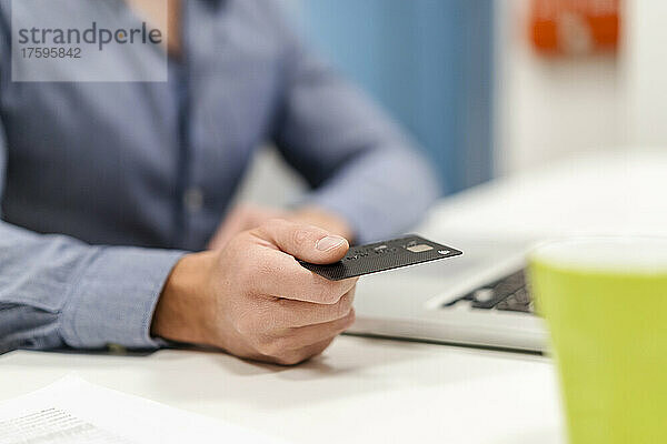 Geschäftsmann mit Kreditkarte per Laptop am Schreibtisch im Büro
