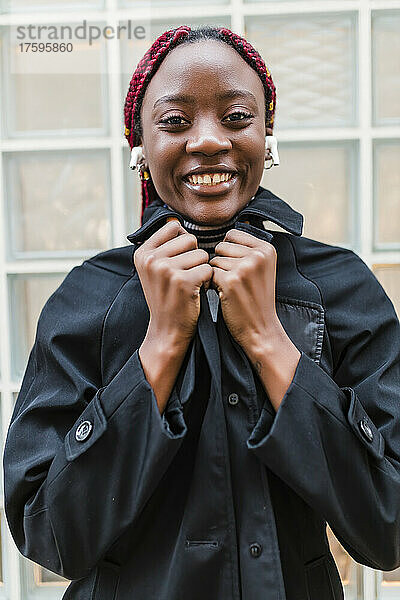 Lächelnde Frau mit kabellosen In-Ear-Kopfhörern in schwarzer Jacke