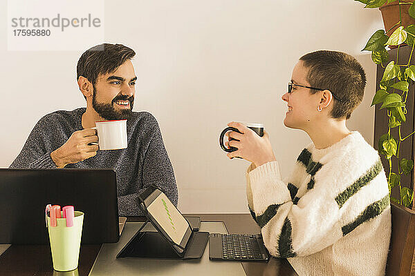 Zufriedene Kollegen trinken Kaffee am Schreibtisch in einem kleinen Büro