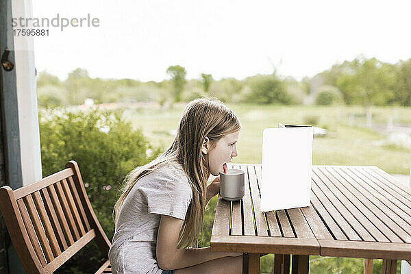 Mädchen leckt Glas und schaut draußen am Tisch auf den Tablet-PC