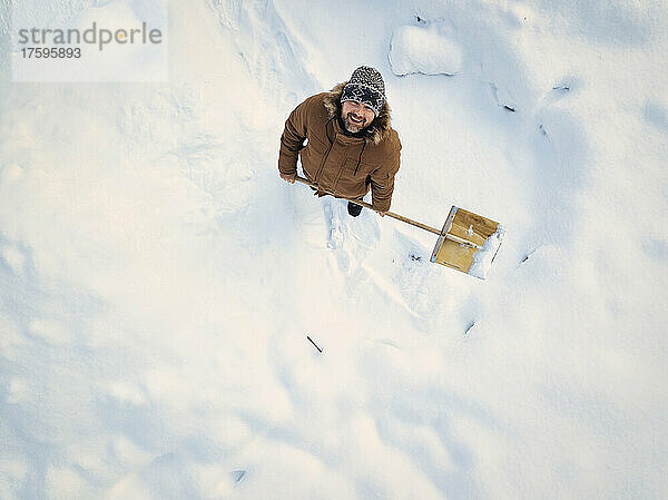 Smiling man holding snow shovel standing on snow in winter