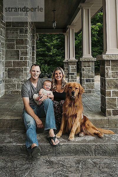 Glückliche Familie mit Hund  der auf der Veranda sitzt