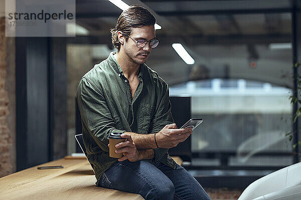 Geschäftsmann sitzt mit Smartphone am Schreibtisch im Coworking-Büro
