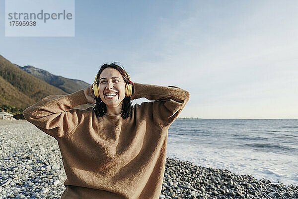 Fröhliche junge Frau genießt Musik über Kopfhörer am Strand