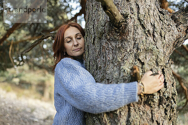 Frau mit geschlossenen Augen umarmt Baum im Park