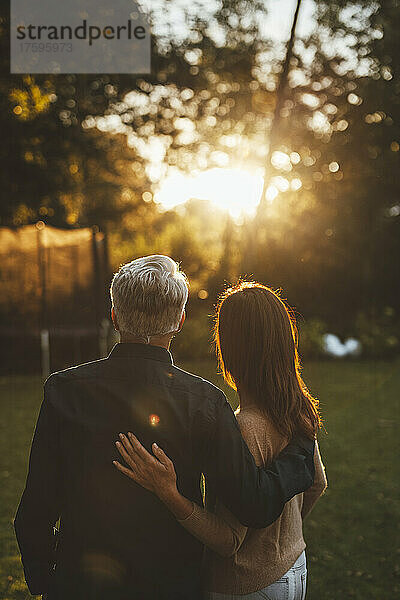 Ein Paar mit umschlungenen Armen steht bei Sonnenuntergang gemeinsam im Hinterhof