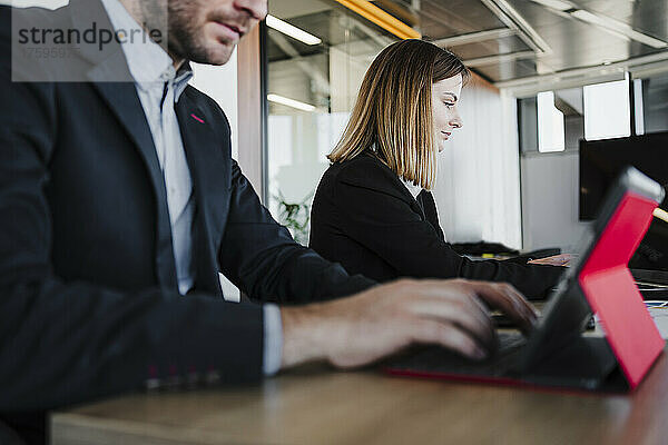 Junge Geschäftsfrau sitzt neben einem Kollegen und nutzt einen Tablet-PC am Schreibtisch im Büro