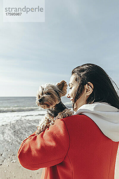 Frau trägt Hund an sonnigem Tag am Strand