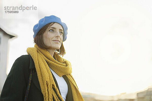 Schöne Frau mit blauer Baskenmütze und gelbem Schal an einem sonnigen Tag