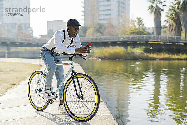 Junger Mann benutzt Smartphone auf Fahrrad am See in der Stadt