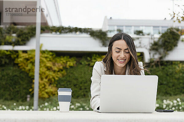 Lächelnde Geschäftsfrau  die im Park am Laptop arbeitet