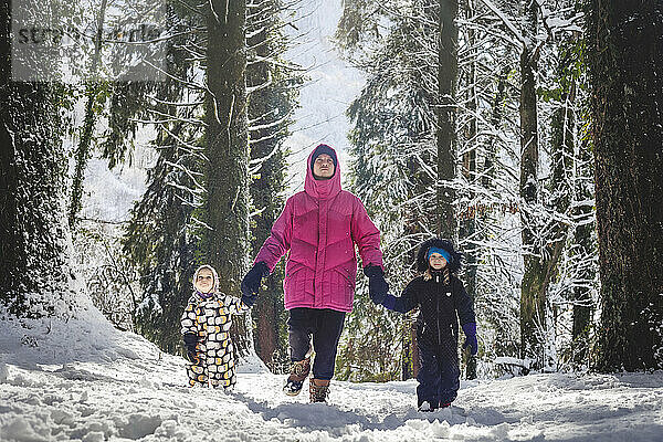 Vater und Töchter gehen an einem sonnigen Tag im verschneiten Wald spazieren
