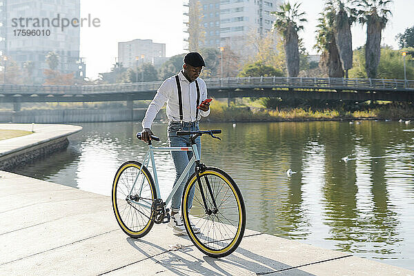 Mann nutzt Mobiltelefon mit Fahrrad auf Fußweg in der Stadt