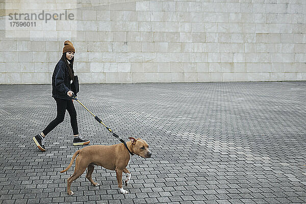 Frau mit Hund läuft auf Fußweg an der Mauer