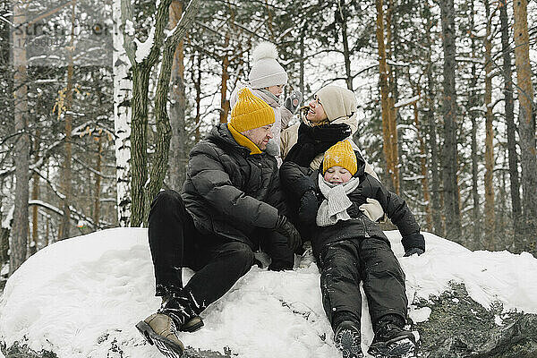 Mann und Frau sitzen mit Tochter und Sohn auf Schnee im Winterwald