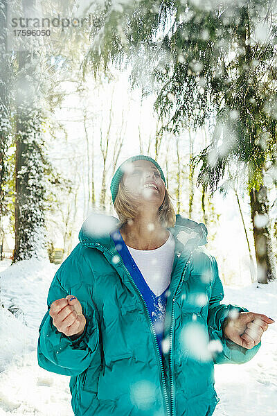 Glückliche Frau genießt Schneefall im Wald