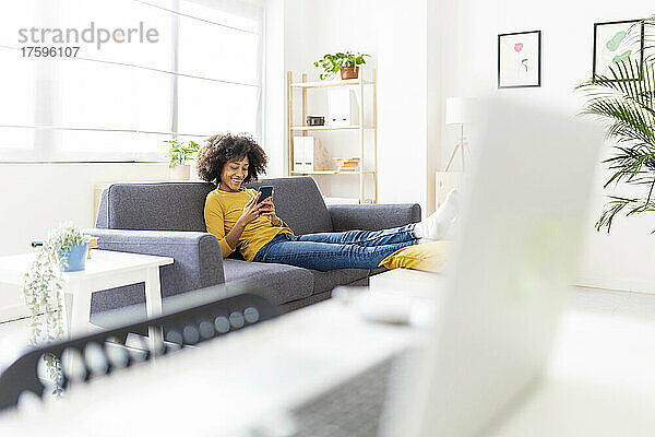 Lächelnde Frau  die im Wohnzimmer mit ihrem Mobiltelefon im Internet surft