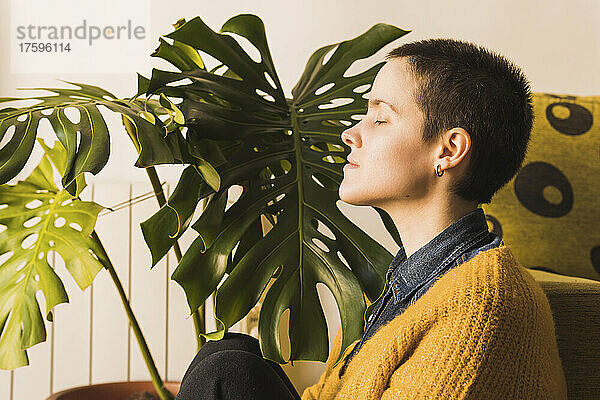 Woman with eyes closed by monstera plant at home