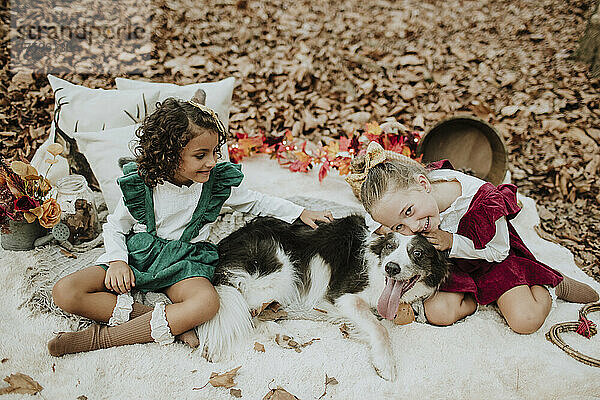 Smiling girls sitting with dog in autumn forest