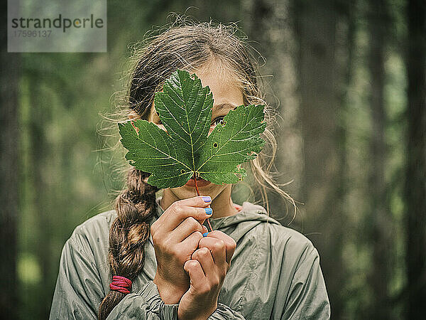 Mädchen bedeckt Gesicht mit grünem Ahornblatt