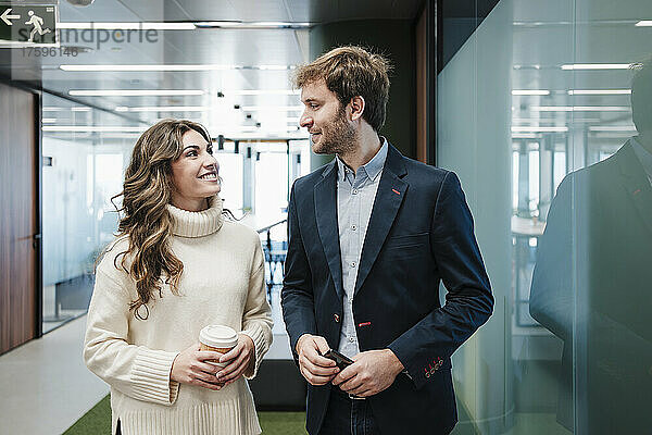 Lächelnder Geschäftsmann und Geschäftsfrau  die einander durch Glaswand im Büro betrachten