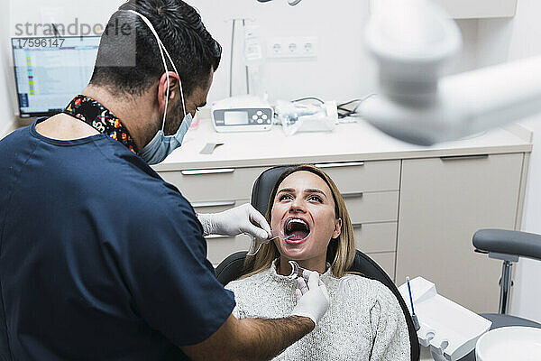Zahnarzt überprüft die Zähne des Patienten im Behandlungsraum der Klinik