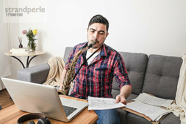 Mann spielt Saxofon und betrachtet Musiknoten im heimischen Wohnzimmer