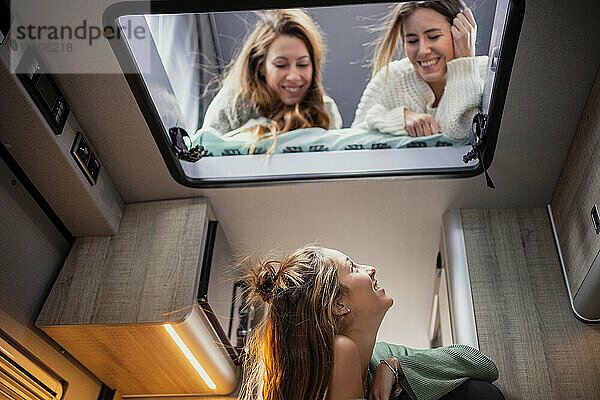 Smiling woman looking at friend on bed in camper van