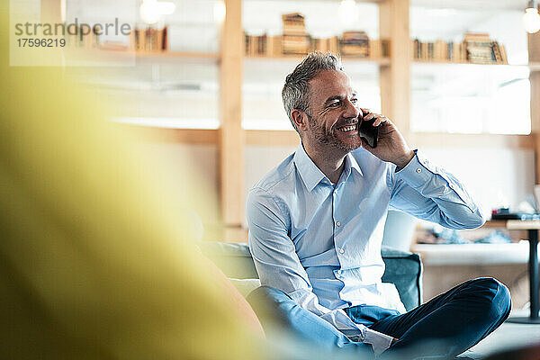 Cheerful businessman talking on mobile phone at workplace