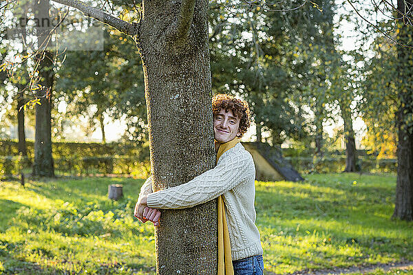 Smiling young man hugging tree at park