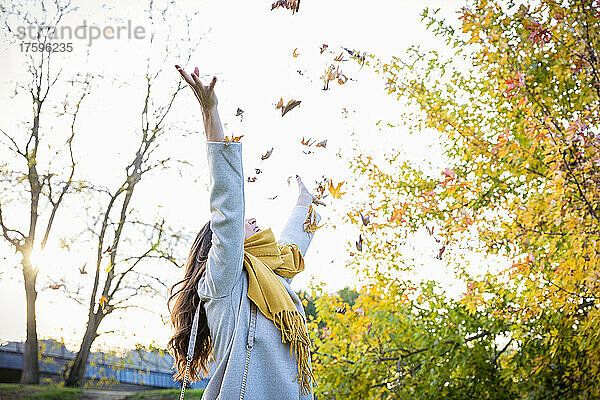 Carefree woman throwing leaves in autumn park