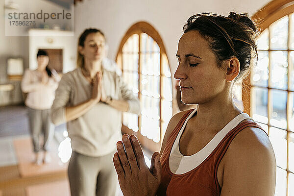 Yoga instructor meditating with hands clasped in class