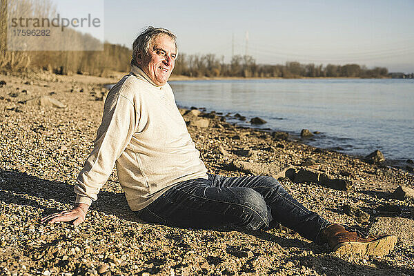 Lächelnder Mann  der an einem sonnigen Tag am Strand sitzt