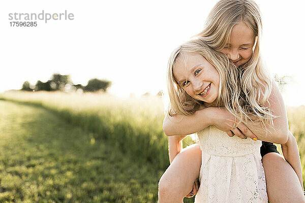 Lächelndes Mädchen trägt Schwester huckepack auf dem landwirtschaftlichen Feld