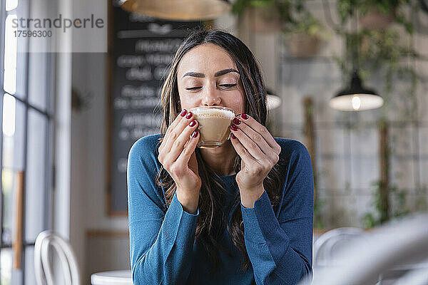 Glückliche Frau trinkt Cappuccino im Café