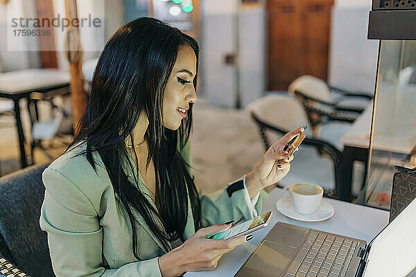 Geschäftsfrau bezahlt mit Kreditkarte auf Smartphone im Café
