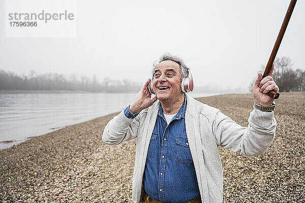 Glücklicher älterer Mann  der über drahtlose Kopfhörer Musik hört und am Strand genießt
