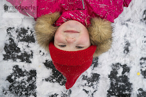 Lächelndes Mädchen mit roter Strickmütze  das im Schnee liegt