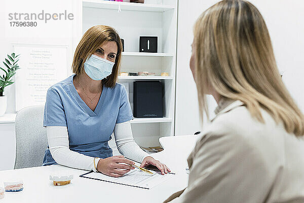 Arzt trägt eine schützende Gesichtsmaske und bespricht mit dem Patienten die Krankenakte in der Klinik