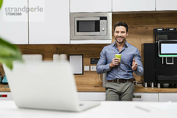 Lächelnder Geschäftsmann bei Videoanruf über Laptop in der Küche