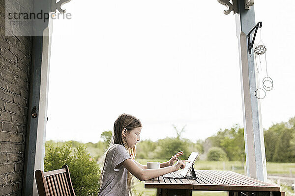 Mädchen benutzt Tablet-Computer auf Tisch auf der Terrasse