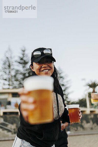 Smiling woman with beer cups standing at beach