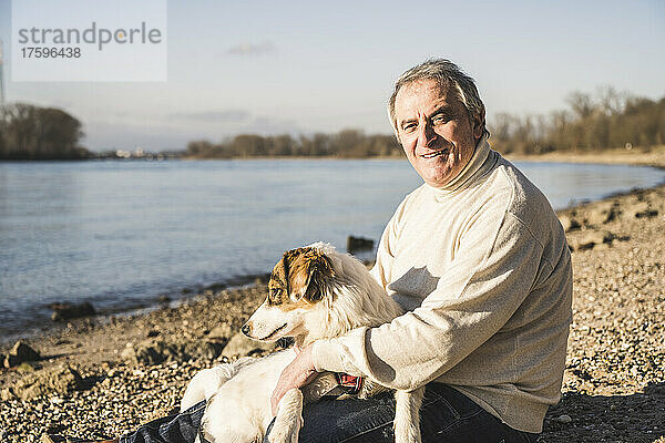 Glücklicher älterer Mann mit Hund  der an einem sonnigen Tag am Strand sitzt