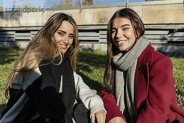 Smiling young friends in warm clothing sitting together on sunny day
